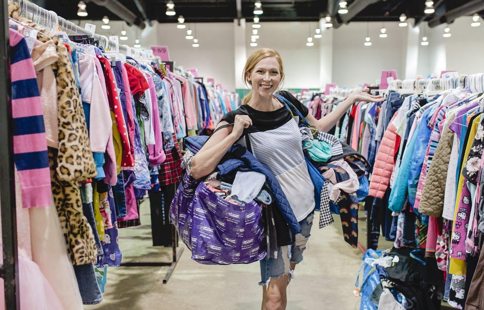 Mom holds hand up to show of rows and rows of clothing for sale at 50 to 90% off retail prices!